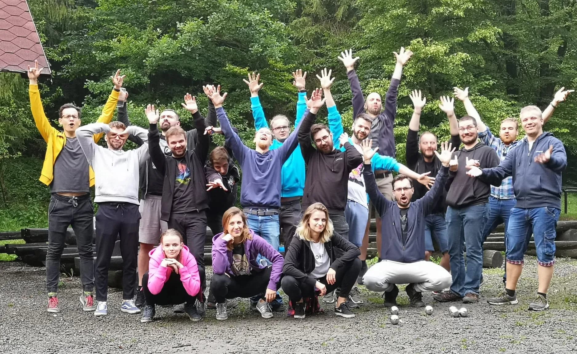 A group of 18 Revolve Healthcare employees looking happy with their hands in the air during an outdoor company retreat