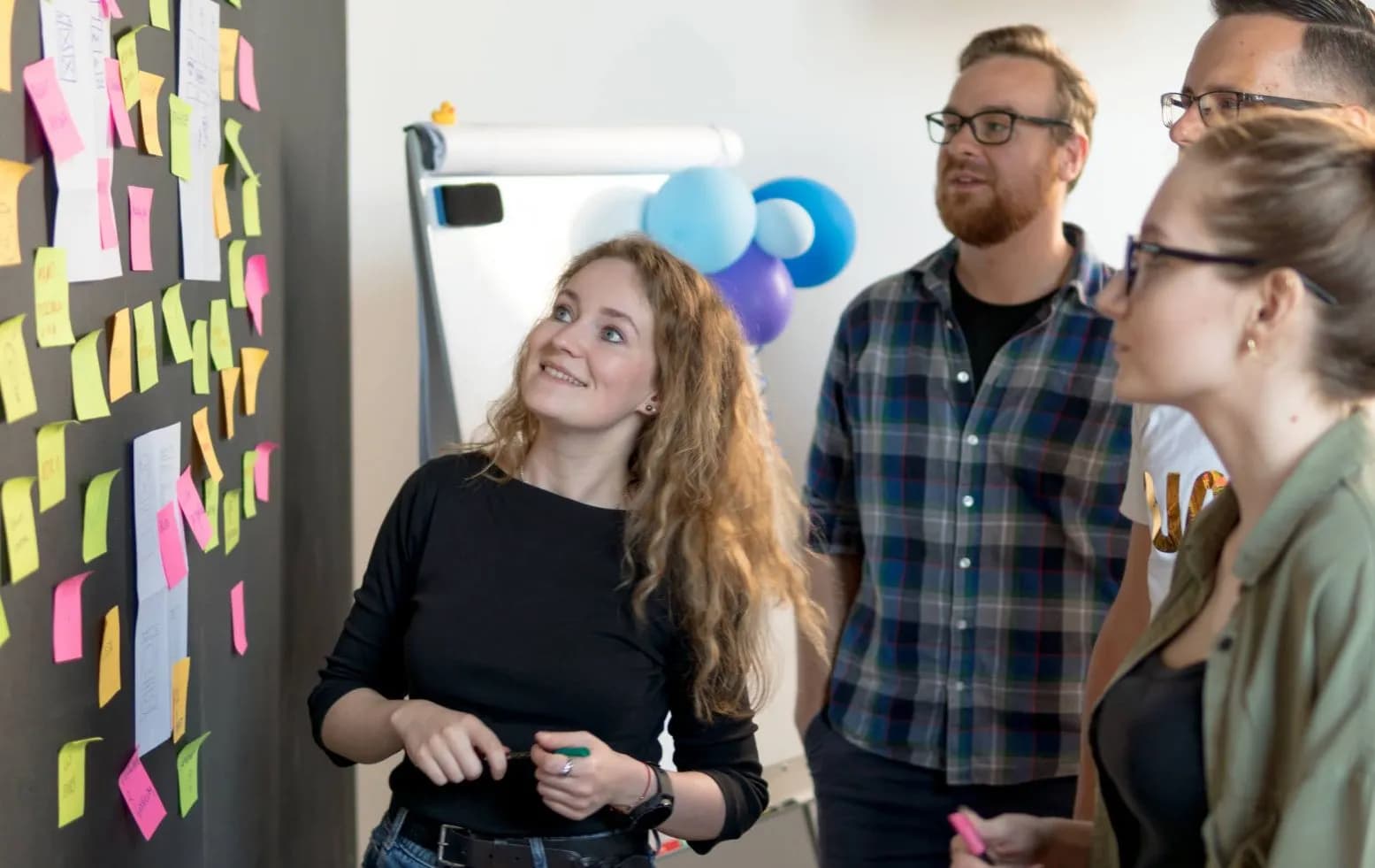 Four people looking at a black wall full of colourful sticky notes after a software development workshop